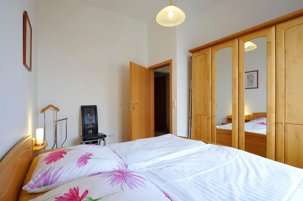 Schlafzimmer mit bezogenem Doppelbett, Nachttischleuchte und großem Spiegelschrank aus hellem Holz