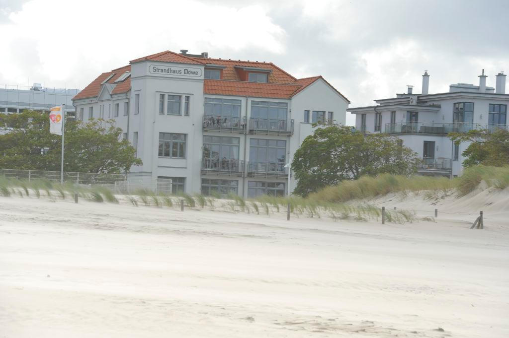 Blick vom Sandstrand über die Dünen auf das weiße Strandhaus Möwe mit rotem Dach